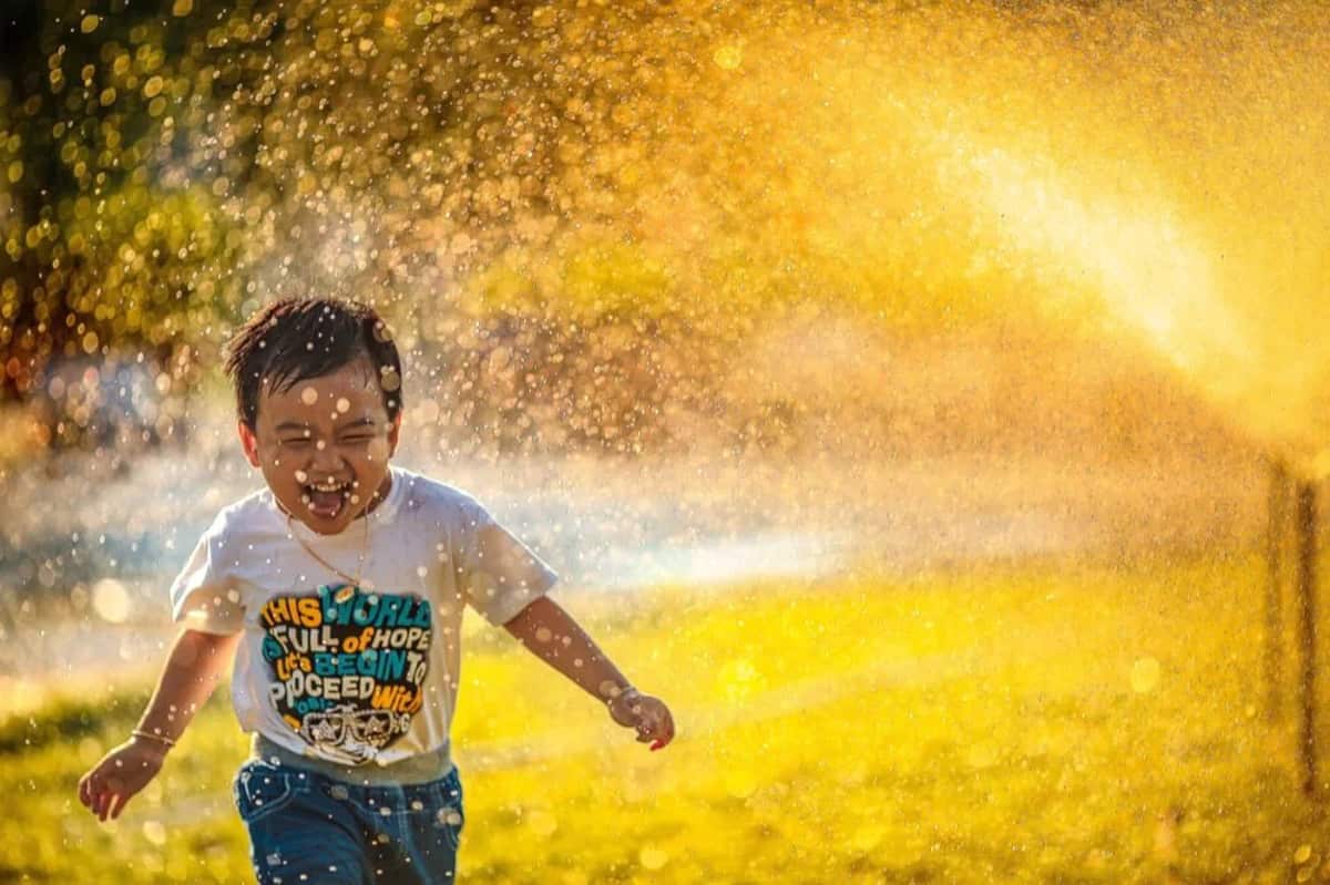 A laughing boy running through a sprinkler on a sunny lawn