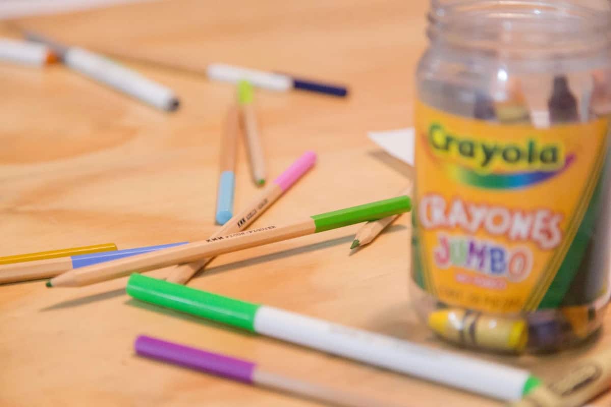 Markers and a jar of jumbo crayons on a wooden table